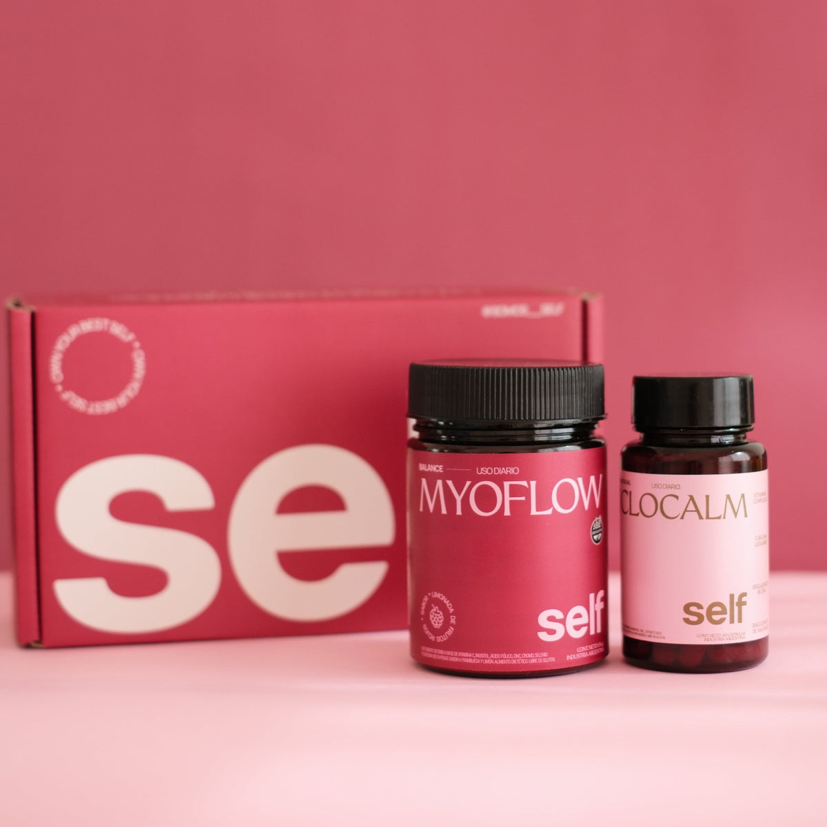 Kit balance (1 myoflow (suplemento en polvo para sop, balance hormonal, resistencia a la insulina) y 1 ciclocalm (suplemento en capsulas para dolor menstrual, inflamación y spm y) caja self de cartón microcorrugado detrás). Fondo plano rosa. 