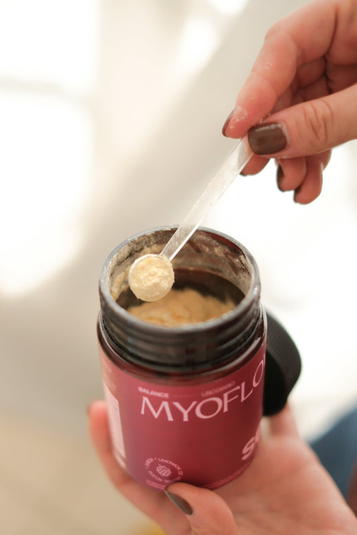 suplemento myoflow (suplemento para sop, resistencia a la insulina y balance hormonal) en polvo, abierto con cucharita medidora. Manos agarrando el producto. 