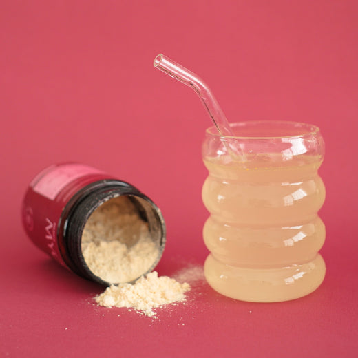 Myoflow (suplemento en polvo a base de inositol para el balance hormonal, sop, resistencia a la insulina) abierto con polvo que sale del pote.Vaso de vidrio con sorbete con el preparado de myoflow + agua dentro. ondo plano rosa.